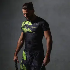 Mężczyzna w czarnym rashguardzie z neonowymi wstawkami, gotowy do treningu. To idealny strój, by poczuć się pewnie i komfortowo.