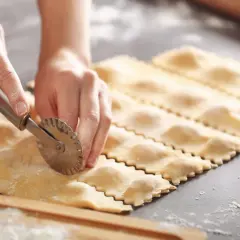 Hände schneiden mit einem Teigrädchen frische Ravioli. So einfach ist ravioli selber machen!