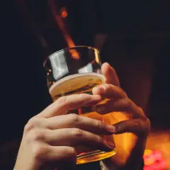Dwie dłonie trzymające szklankę piwa, w tle rozmyte światła i chorągiewki. Czy piwo tuczy?