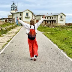 Persona con los brazos en alto camina por un camino hacia un faro y edificios. Parece una estaca de bares, pero es un lugar histórico.