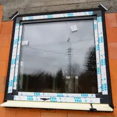 Nowy węgarek okienny w trakcie montażu, otoczony ceglanym murem i pianką izolacyjną.