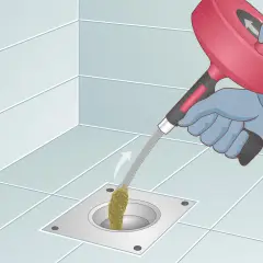 Gloves on, a drain snake is used to clear a clog from a shower drain. This shows how to snake a drain effectively.