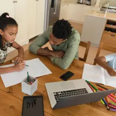Familie lernt zu Hause. Ist Homeschooling in Deutschland erlaubt? Kinder schreiben und malen, Vater hilft.