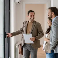 Agent ouvrant une porte à un couple, discutant des risques à acheter un bien loué.