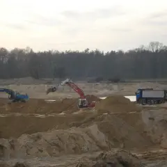 Koparki i wywrotka pracują na placu budowy, wykonując prace ziemne.