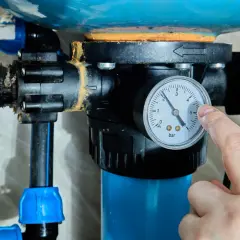 Palec wskazuje manometr przy hydroforze, pokazując ciśnienie. Dowiedz się, jak odpowietrzyć hydrofor, by działał sprawnie.