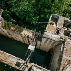 Widok z lotu ptaka na betonową śluzę Leśniewo Górne, otoczoną bujną zielenią. Woda w kanale jest ciemna, a na budowli widać ślady czasu.