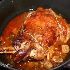 Une succulente épaule d'agneau rôtie dans sa cocotte, baignant dans un jus savoureux avec des oignons et des carottes.