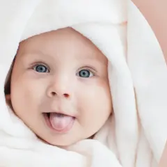 Urocze dziecko z niebieskimi oczami owinięte w biały kocyk, wystawiające język.