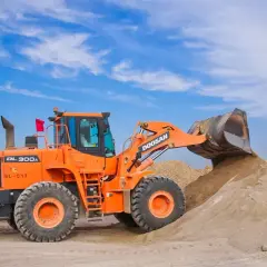 Pomarańczowa ładowarka Doosan DL300A zasypuje kopiec piasku, który może posłużyć jako żwir do betonu.