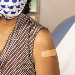 Osoba z maską na twarzy i plastrem na ramieniu po szczepieniu. Choć hpv szczepionka skutki uboczne są rzadkie, warto być świadomym.