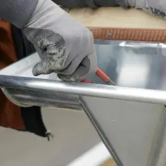 Hand mit Handschuh dichtet Dachrinne mit Werkzeug ab.