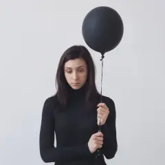 Donna con palloncino nero, espressione malinconica. Potrebbe rappresentare l'anedonia significato, la perdita di piacere.