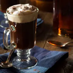 En värmande irish coffee med vispad grädde och kanel på en blå duk.