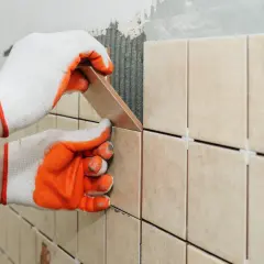 Hands in gloves carefully place a tile, demonstrating how to tile a shower floor.