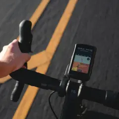 Dłoń trzymająca kierownicę roweru z zamontowanym licznikiem GPS pokazującym mapę.