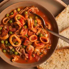 Calamari al sugo con piselli, un piatto saporito servito in una ciotola con pane tostato.