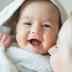 La alegría contagiosa cuando empieza a reírse un bebé, envuelto en una toalla blanca, con una madre dándole un beso.
