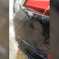 Usuwanie wgnieceń gorącą wodą na czarnym zderzaku samochodu. Woda spływa po uszkodzonym fragmencie.