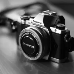 Prześwietlone zdjęcie aparatu Olympus OM-D. Srebrno-czarny korpus i obiektyw z napisem "OLYMPUS".