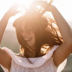 Lachende Frau mit fliegenden Haaren im Sonnenlicht. Ein Gefühl von Freiheit, das auch in den Wechseljahren möglich ist.