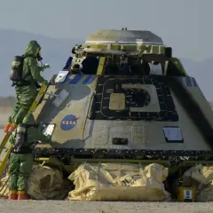 Zespół w zielonych kombinezonach ochronnych bada kapsułę kosmiczną NASA na pustkowiu.