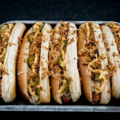 Sechs Hot Dogs in einem Blech, belegt mit Gurken, Sauerkraut, Senf und knusprigen Zwiebeln – die perfekten Hot Dog Zutaten für jeden Geschmack.