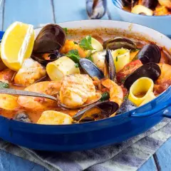 Caldereta de pescado humeante en cazuela azul, con gambas, mejillones, trozos de pescado blanco y limón.