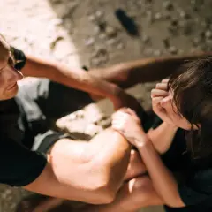 Un uomo con lunghi capelli biondi guarda una donna che gli tocca il braccio. Sono seduti sulla sabbia.