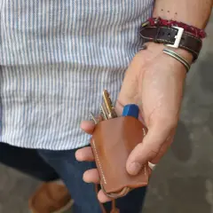 Main d'un homme au style workwear, tenant un étui à clés en cuir marron.