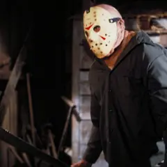 Postać w masce hokejowej, z maczetą w ręku, groźnie wygląda w mroku. Klasyczny slasher horror.