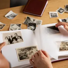 Wspomnienia wracają podczas wklejania zdjęć do albumu. Na stole leżą stare fotografie, a ręce starannie układają je na białych kartach.