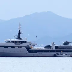 Lo yacht Koru, con il suo elicottero pronto al decollo, naviga maestoso in acque tranquille, con le montagne sullo sfondo.