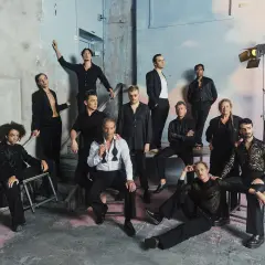 Ensemblen från Dramaten poserar i en rå miljö. En del sitter, andra står, alla klädda i svart. Kanske en scen ur ett arv efter Dramaten.