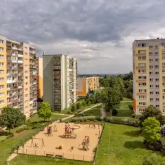 Bloki mieszkalne z placem zabaw na pierwszym planie, pod pochmurnym niebem.