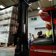 Operator wózka widłowego przygotowuje transport drobnicowy. Na paletach leżą paczki owinięte folią.