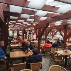 Zadaszony ogródek restauracyjny z drewnianymi belkami, lampami i siedzącymi przy stołach ludźmi.