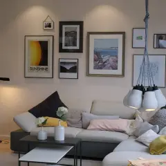 Ściana nad sofą ozdobiona jest galerią obrazów w różnych **painting styles**: od retro plakatu "Sunshine" po akwarelowy pejzaż morski.