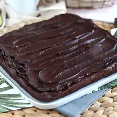 Puszysty brownie z awokado, polane błyszczącą polewą czekoladową. Obok połówka awokado i kawałek gorzkiej czekolady.