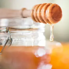 Ein Holzlöffel tropft goldenen Akazienhonig in ein Glas. Dieser Honig ist nicht nur süß, sondern auch gesund.