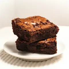 Dwa wilgotne kawałki ciasta brownie z płynną czekoladą, ułożone na białym talerzyku.
