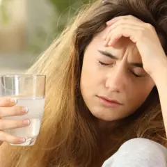 Kobieta z bólem głowy i szklanką wody. Czy opioidy to tylko leki przeciwbólowe?