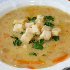 Aksamitna zupa cebulowa z grzankami i natką pietruszki, podana w białej misce.