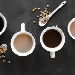 Vier Tassen Kaffee, zwei schwarz, zwei mit Milch, und Löffel mit Kaffeebohnen. Ein gemütlicher Tee-Teein-Moment.