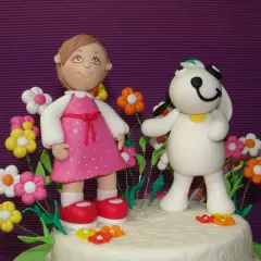 Figuras de porcelana fría: niña con vestido rosa y perro blanco rodeados de flores y un arcoíris.