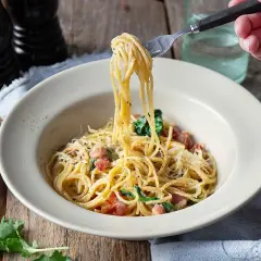 En gaffel lyfter en portion krämig spaghetti carbonara från en skål. Ett perfekt pasta carbonara recept för en god middag.