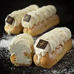 Trois éclairs chantilly généreusement garnis de crème fouettée, ornés d'un carré de chocolat, saupoudrés de sucre glace.