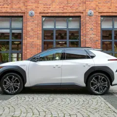 Biały Toyota bZ4X elektryczny SUV stoi na brukowanej ulicy przed ceglanym budynkiem z dużymi oknami.