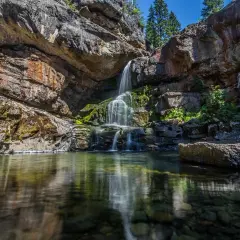 Cascadas en León, agua cristalina cae sobre rocas cubiertas de musgo, reflejándose en un estanque sereno.