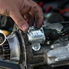 Mechanik naprawia rozrusznik w aucie, przykręcając śrubę.